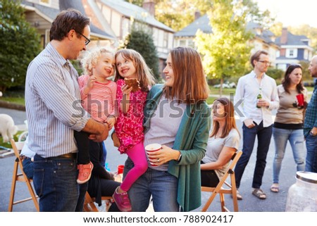 Parents holding their young kids while they eat at a block party