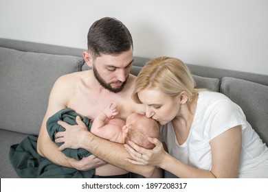 Parents Hug A Crying Newborn Baby At Home. Dad Holds His Newborn Son Trapped In A Trendy Green Muslin Diaper Skin To Skin. Mom Gently Kisses The Screaming Baby. Baby Care Concept, First Month Of Life.