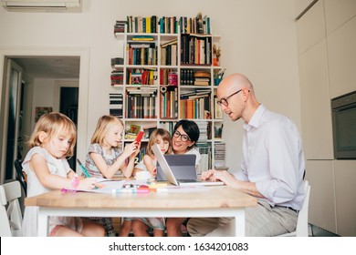 Parents indoor sitting table homeschooling with three female children - mentoring, teaching, education concept