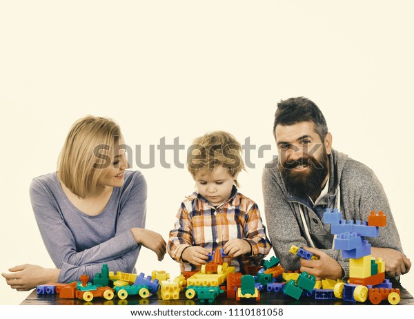  . Parents and kid in playroom. Kindergarten and\
family concept. Family with happy faces build toy cars out of\
colored construction blocks.