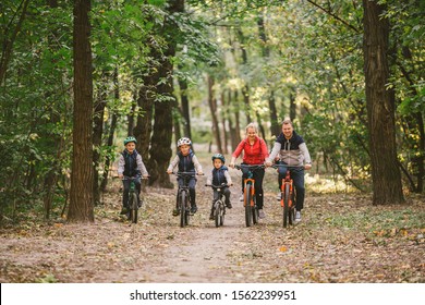 Parents And Kids Cycling On Forest Trail. Young Family Cycling In Autumn Park. Family Mountain Biking On Forest. Theme Family Active Sports Outdoor Recreation. Family Cycling Through Fall Woodland.