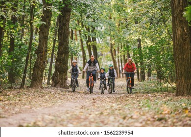 Parents And Kids Cycling On Forest Trail. Young Family Cycling In Autumn Park. Family Mountain Biking On Forest. Theme Family Active Sports Outdoor Recreation. Family Cycling Through Fall Woodland.