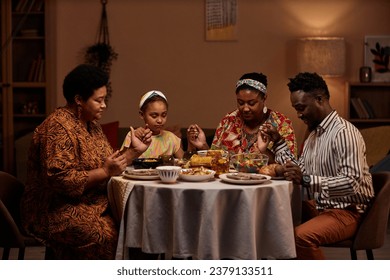 Parents and kids gathered around table, praying together as they share meal - Powered by Shutterstock