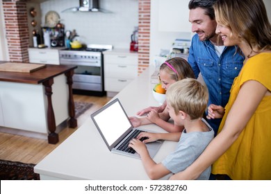 Parents And Kids Using Laptop In Kitchen At Home