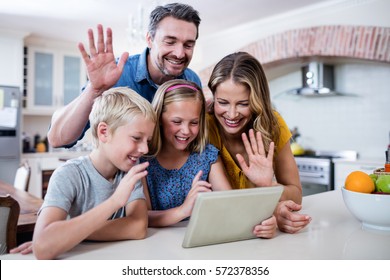 Parents And Kids Waving Hands While Using Digital Tablet For Video Chat In Kitchen