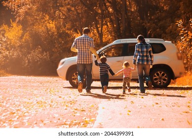 Parents - Mother, Father And Kids - Daughter, Son Holding Hands Each Other Against White SUV Big Car. Outdoor Photo In Autumn Park. Casual Dress. Sunset Light Rays