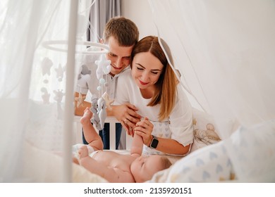 parents near a newborn baby lies in a white crib with canopy. furniture for the children's room. the happiness of motherhood. goods for children.