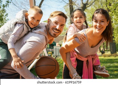 Parents playing with their children in the park with basket ball. Looking at camera.