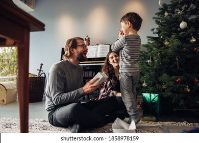 Parents presenting gift to their son sitting beside a Christmas tree. Boy looks excited while getting Christmas gift. - Powered by Shutterstock