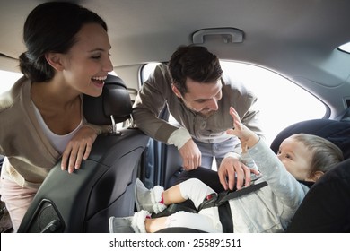 Parents securing baby in the car seat in their car