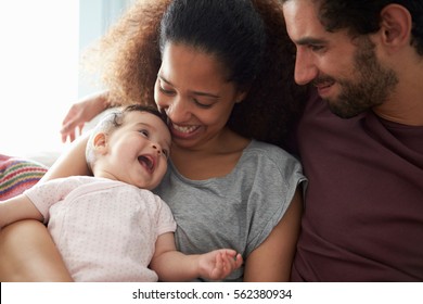 Parents Sitting On Sofa Cuddling Baby Daughter At Home