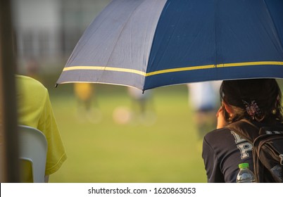 Parents Sitting And Watching Their Son Playing Football In A School Tournament On A Clear Sky And Sunny Day. Sport, Outdoor Activity With Lifestyle And A Happy Family. Soccer Mom & Dad Concept.