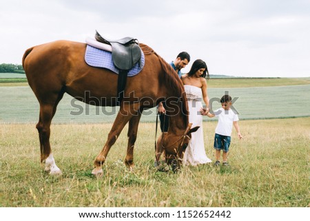 parents and son standing near beautiful brown horse on field
