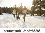 Parents take children on sleds while happily walking along snowy path in winter park. Man pulls sled with his son and daughter and smiling woman follows them. Concept of family winter fun.