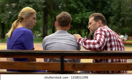 Parents Talking With Son On Bench In Park, Supporting Teen In Time Of Trouble