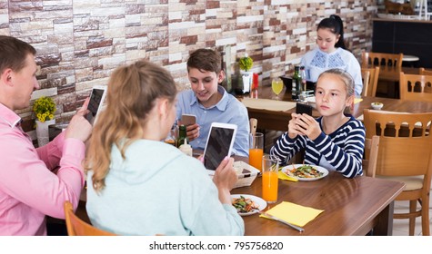 Parents With Teenage Children Having Dinner In Cafe And Phubbing