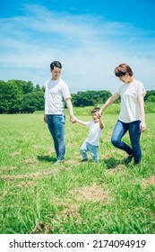 Parents And Their Child Holding Hands And Walking On A Sunny Green Space