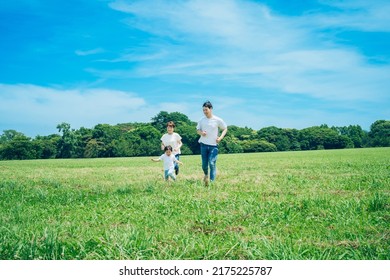 Parents And Their Child Running Around The Meadow