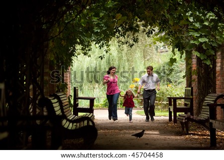 Parents together with daughter run on tunnel from ivy in summer garden.