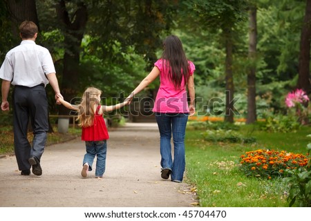 Parents together with daughter walk on summer garden. Leave afar keeping for hands.