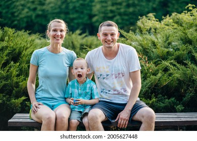 Parents and twins boy and girl sitting on wooden bridge in a park. Sunny day, good mood. Happy joyful young family father, mother and little son having fun outdoors, playing together in summer.