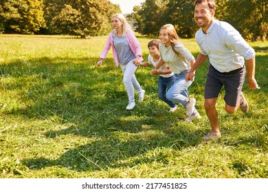 Parents and two children run together across a meadow in the park in nature in summer - Shutterstock ID 2177451825