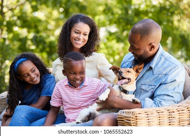 Parents And Two Kids Sitting With Pet Dog In The Garden