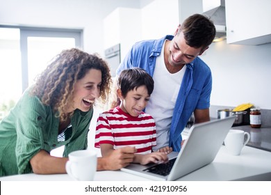 Parents using laptop with son in kitchen at home