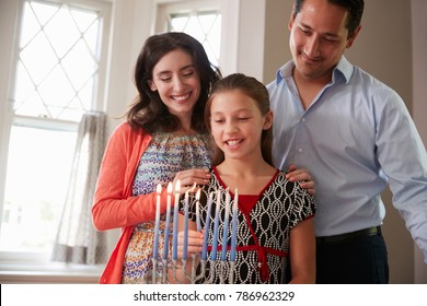 Parents Watch Daughter Light Candles On Menorah For Shabbat