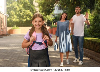 Parents Waving Goodbye To Their Daughter Before School Outdoors