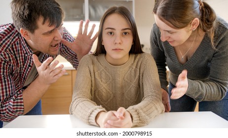 Parents Yelling And Shouting At Teenage Daughter Sittin Behind Table And Looking In Camera