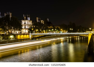 Paris By Night. The Seine And The City In The Background. On The Left The Wake Of A Boat Darting Across The River. Photo Taken With Long Exposure.