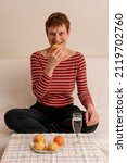 Paris, France - 01 28 2022: A woman drinking champagne and eating gougere sitting on a sofa at home