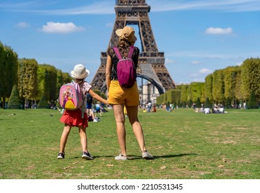 Paris, France - 27 August 2022: Mom And Daughter In Panama Hats And Backpacks Stand On The Champ De Mars And Look At The Eiffel Tower On A Sunny Summer Day.