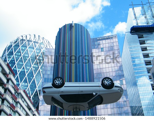 Paris, France - 8 13 2019: giant contemporary\
art at La Defense, Paris. Upside down car in front of colorful\
pipes and buildings.
