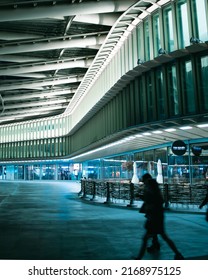 Paris, France. April 23rd, 2022. A Person Walking In An Outdoor Mall With Rows Of Glass Windows At Night. 