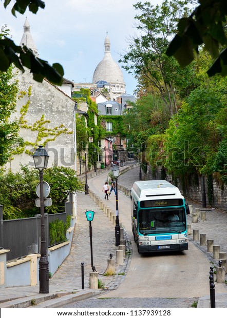 Paris / France — August 18, 2015: a RATP bus\
on the hill of Montmartre, Paris, France, with the dome of\
Sacre-Coeur basilica in the\
background