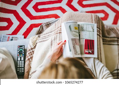 PARIS, FRANCE - AUGUST 24, 2014: View from above of woman reading IKEA Catalogue before buying new curtains for her new house. Tilt-shift lens used