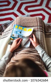 PARIS, FRANCE - AUGUST 24, 2014: View from above of woman covered with blanket reading IKEA Catalogue opening the cover page choosing the best furniture - tilt shift lens