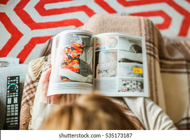 PARIS, FRANCE - AUGUST 24, 2014: View From Above Of Woman Reading IKEA Catalogue Before Buying Kitchen Furniture For Her New House.