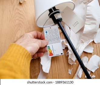 Paris, France - Dec 13, 2020: POV Male Hand Holding Paper Tag Of A Zara Home Table Elegant Lamp With Ecological Energy Efficiency Bulb Recommendations A And A Plus