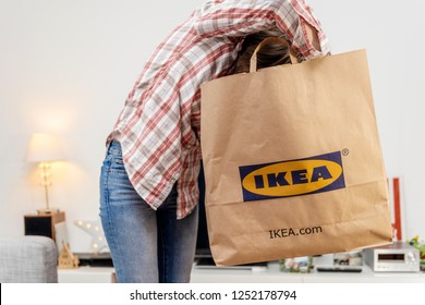 PARIS, FRANCE - DEC 2, 2018: Casual dressed woman holding big paper IKEA bag full with merchandise from the famous swedish furniture retailer - head in the bag searching for object