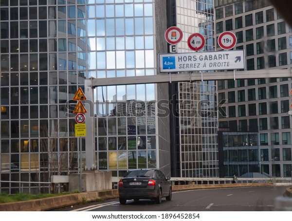 Paris, France - Dec. 2020 - A car driving at\
a crossroads, on a road that crosses La Défense, the French\
capital\'s financial district and the largest in Europe, at the foot\
of glass skyscrapers