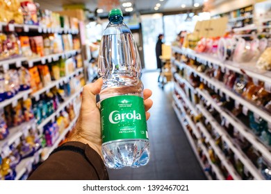 Paris, France - Dec 27, 2017: Man Hand POV Personal Perspective Holding Carola Mineral Water In Modern Supermarket With Multiple Product On The Shelves