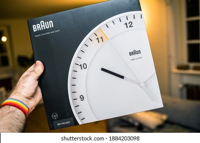 Paris, France - Dec 8, 2020: POV Personal Perspective Male Hand Holding Package Of New Braun BC17F-DCF- Radio Controlled Wall Clock Traditional German Design By Dieter Rams - Living Room Background