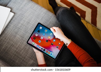 Paris, France - Feb 12, 2019: Overhead view of elegant woman holding new iPad pro tablet by Apple Computers on the couch in living room looking at home screen apps