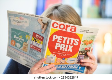 Paris, France - Feb 23, 2022: Woman reading Cora hypermarket special offer leaflet flyer choosing best prices with large text Petit Prix translated as Small prices