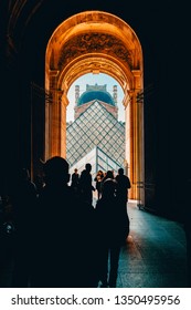 Paris / France - February 16 2019: A Stunning Photo Of Le Louvre Pyramid, As Seen Through A Hallway Of The Museum, With Silhouettes In The Foreground