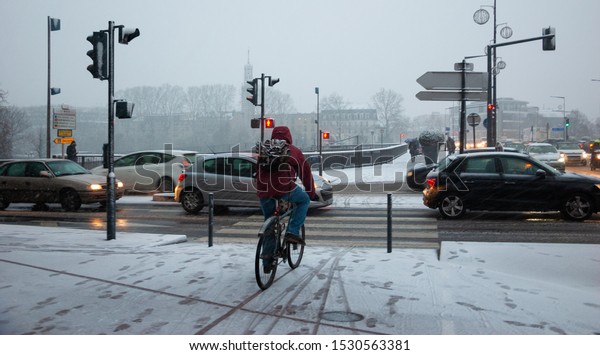 PARIS, FRANCE - FEBRUARY 6, 2018: Parisian\
suburbs under snow in rare snowy day in winter. Cars cross bridge;\
man cycling on bike path covered with snow and Maison-Alfort\
cityscape at background.