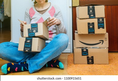 PARIS, FRANCE - JAN 13, 2018: Stack of Amazon Prime packages delivered to a home door woman unboxing one of the small boxes. Amazon is the largest internet based retailer in the United States 